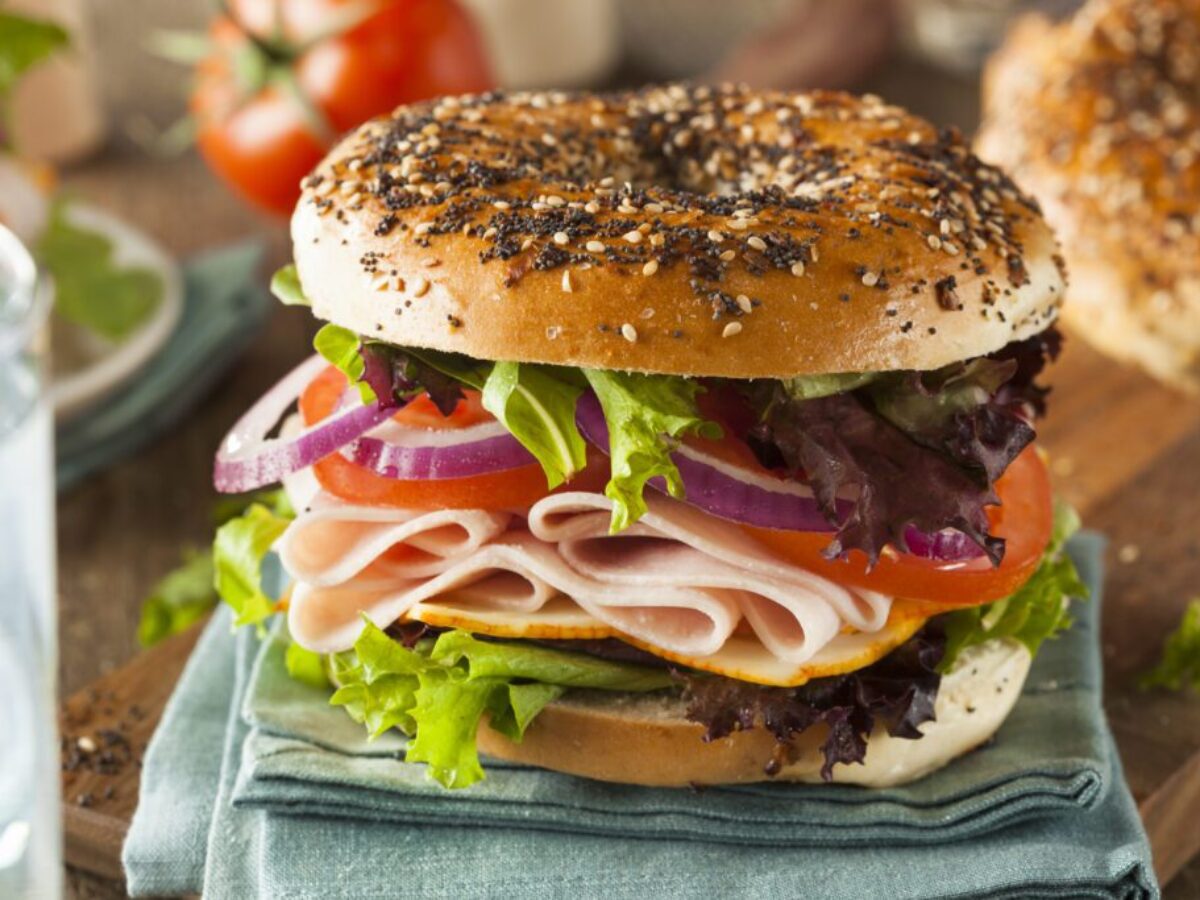 Close-up of a bagel sandwich with onion, tomato, ham, and spring mix.