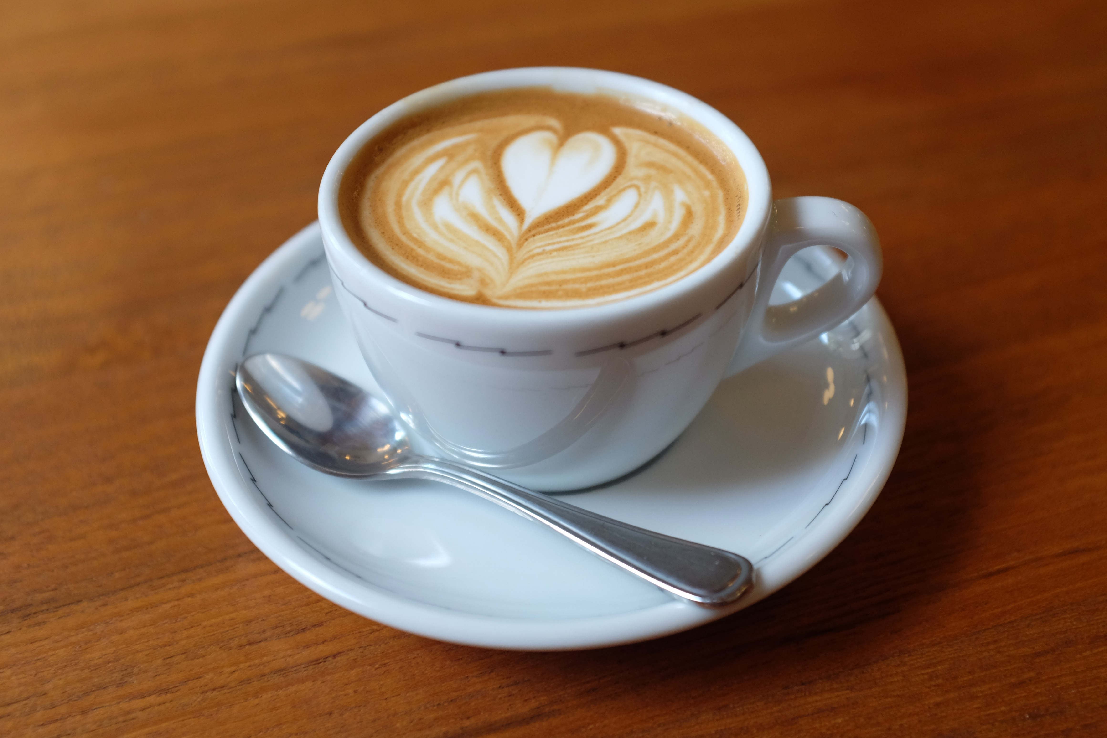 Capuccino served in a  mug on a plate with a spoon.